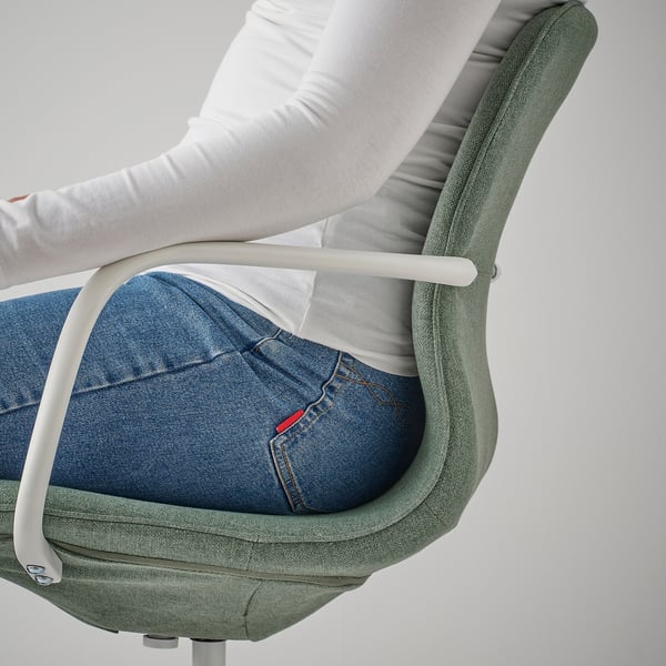 Close-up of a person sitting in a green office chair with height-adjustable seat and tilt mechanism.