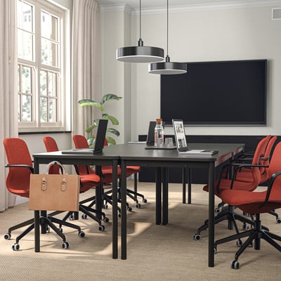 Modern office space with black table, red LÅNGFJÄLL chairs, large screen, and large window. Lighting fixture hangs above.