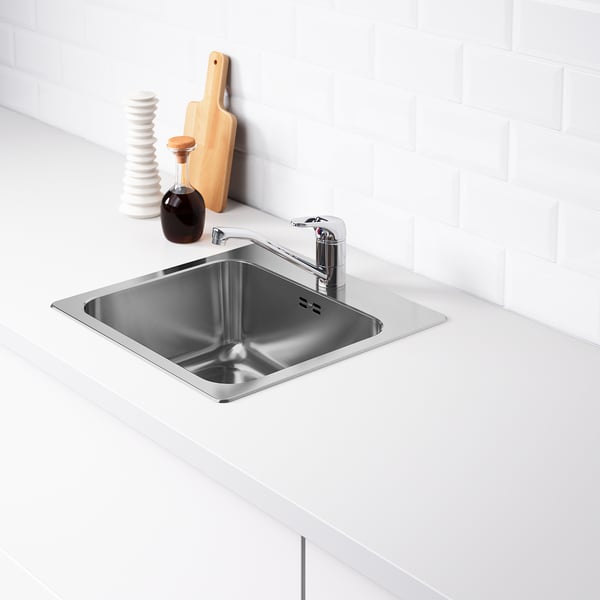 Stainless steel sink with chrome tap, set into white countertop. Back edge is deeper for storage.