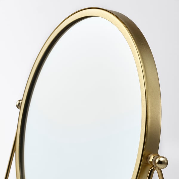 Round gold-framed makeup mirror with magnifying side, reflecting quality craftsmanship.