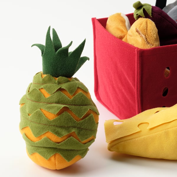 Soft toy pineapple with bright colours and detailed stitching, next to a plush shopping basket with play food.