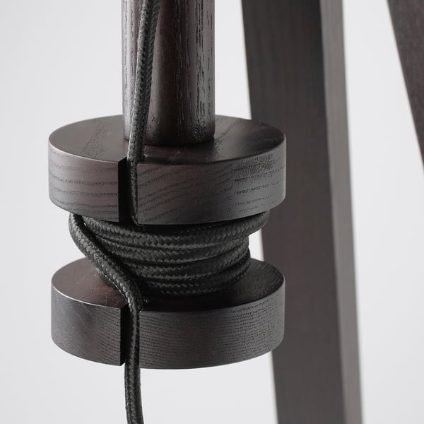 Dark wooden pole lamp with adjustable height, featuring coiled cord storage within its base, designed for organised and flexible use.