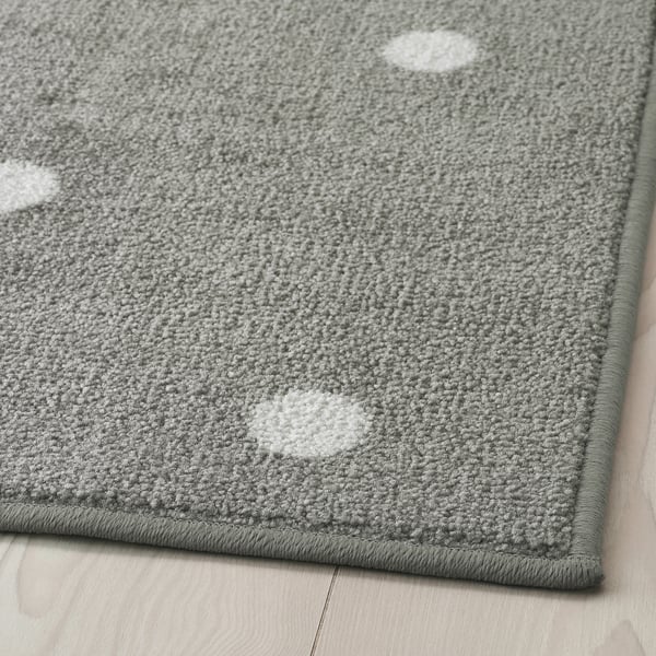 Grey rectangular rug with white dots, laid on a wooden floor, featuring a durable, textured surface and secure rubber backing.