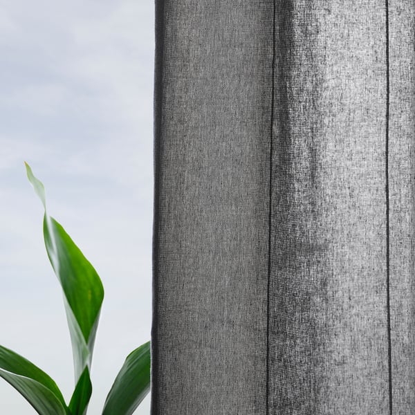 Close-up of dark grey striped curtain near green leaf.