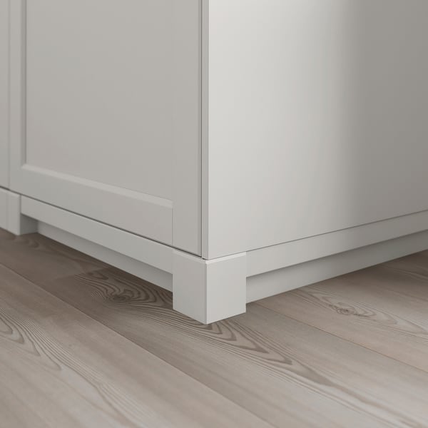 A close-up of a white wooden kitchen cabinet leg with a light, grey-toned wooden floor.