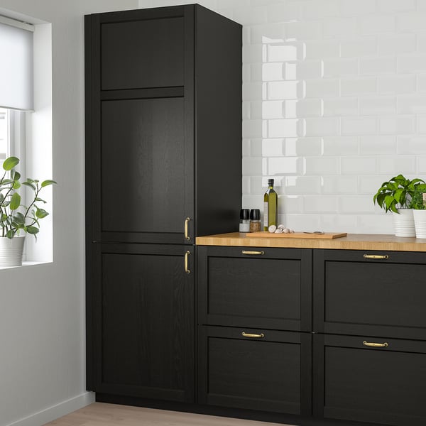 Modern kitchen with tall black LERHYTTAN cabinet, wooden counter, gold handles, bottle, plants, and tiled wall. Tall cabinet dominates scene.