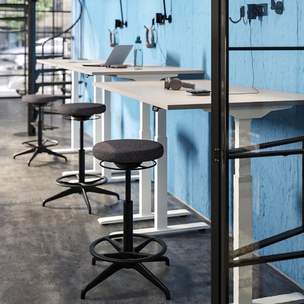 Modern office with LIDKULLEN stools, grey, circular seats, high adjustable desks, and blue walls.