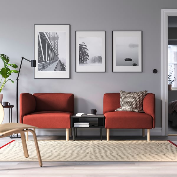 Modern living room with orange sectional sofa, grey wall art, coffee table, lamp, plant, and rug.