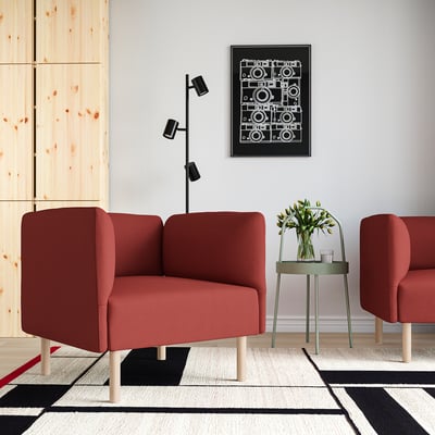 A red LILLEHEM sofa with two chairs, a green side table, black wall lamp, and multicoloured rug against a light wall. Contemporary cosy vibe.