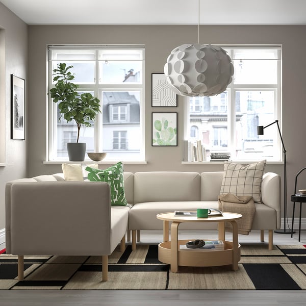 Modern living room with a lillem l-shaped beige sofa, wooden coffee table, large window, hanging light, plant, and rug.
