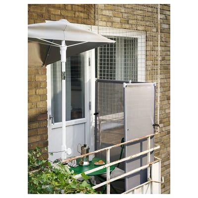 Balcony setup with white LILLEÖ parasol, green table, chairs, and netting against brick wall.