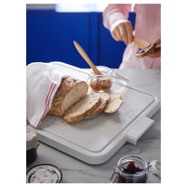 A person spreads jam on bread slices on a LILLHAVET cutting board with rubber feet.
