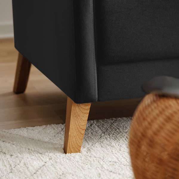 A modern black couch with light wooden legs sits on a white shaggy rug. Next to it, a brown woven basket.