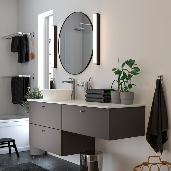 Modern bathroom with LINDBYN mirror, grey countertop, white sink, silver fixtures, green plant, and black towels.