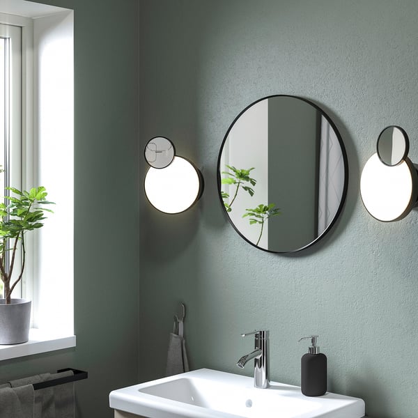 Modern bathroom with round LINDBYN mirror, white sink, and green plant.