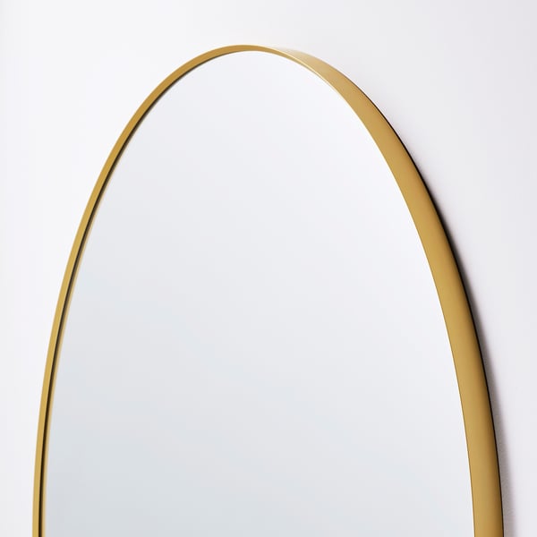 Image shows an elegant, round mirror with a smooth gold frame, reflecting a white wall, indicating high-quality finish and design.