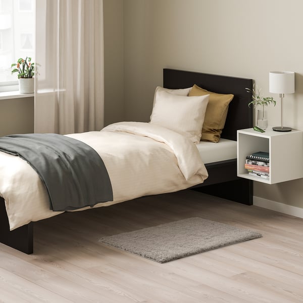 Bedroom with LINDKNUD beige rug, white bed, black headboard, and bedside table with lamp. Rug is small, fitting under bed.