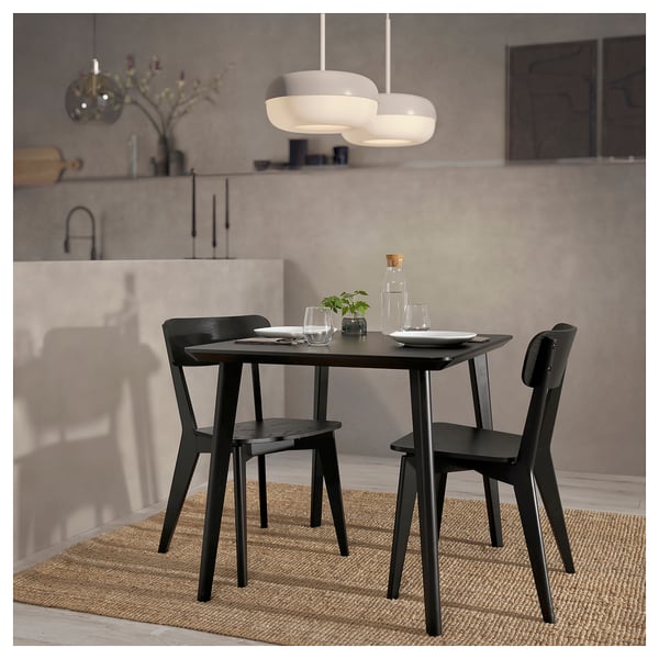 Modern dining set with dark wood table and chairs, pendant light, plates, glasses, and a small plant.