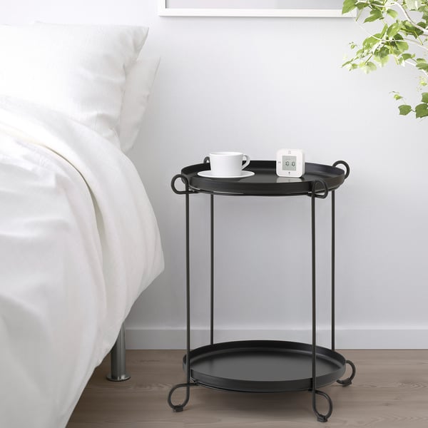 Black side table with trays in minimalist bedroom, holding cup and gadget.