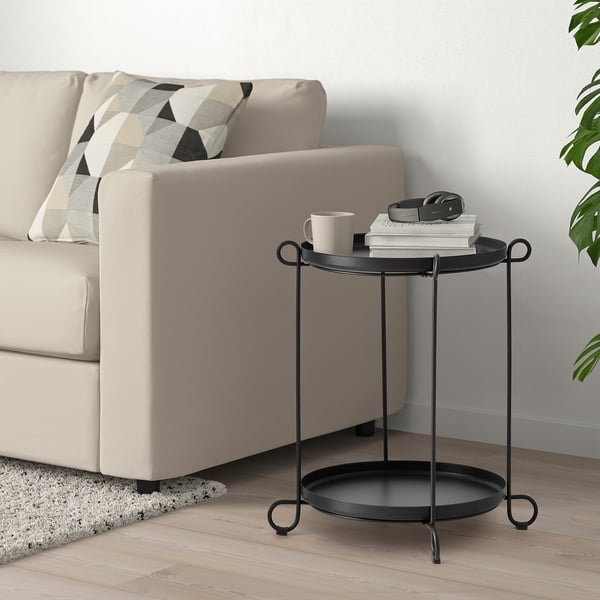 Black LIVELYCKE side table with trays next to sofa, holding mug, books, headphones.