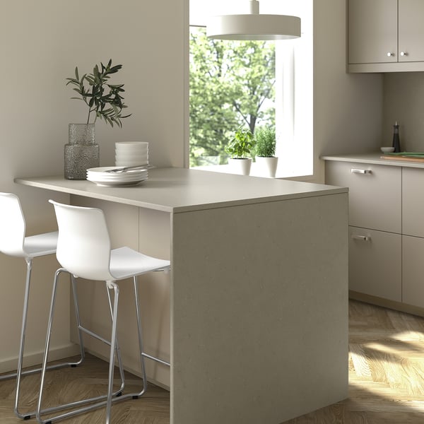 Modern kitchen island with LOCKEBO white recycled glass counter, two white stools, plates, plant, pendant light, and cabinets.