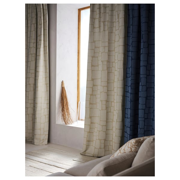 Three LÖNNSTÄVMAL curtains in beige, gray-beige, and navy hang by a window. Beige has a subtle pattern. Light rug with woven texture on floor.