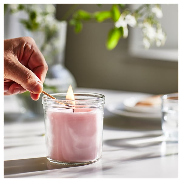 Hand lighting pink scented candle in glass jar.