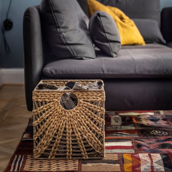 Wicker basket on colourful rug near grey couch.