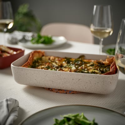 Beige LYCKAD oven dish with food, wine glasses, and plates on a table.