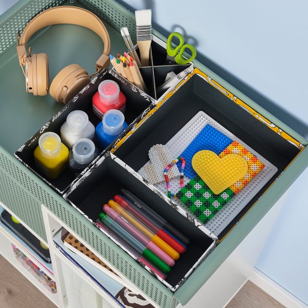 Organised kids storage with art supplies, showing four compartments holding markers, paints, and building toys on a green table.