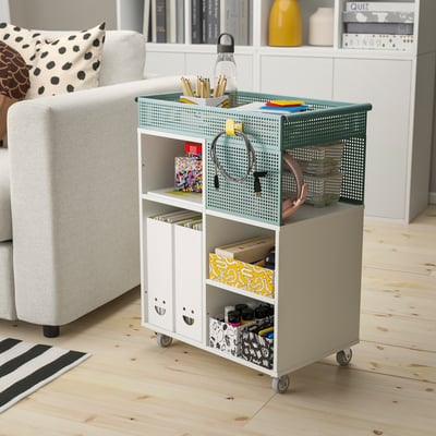Minimalist home office with LYSMASK storage unit. Four green/white boxes on wheels, storing office supplies neatly near a chair and bookshelf.
