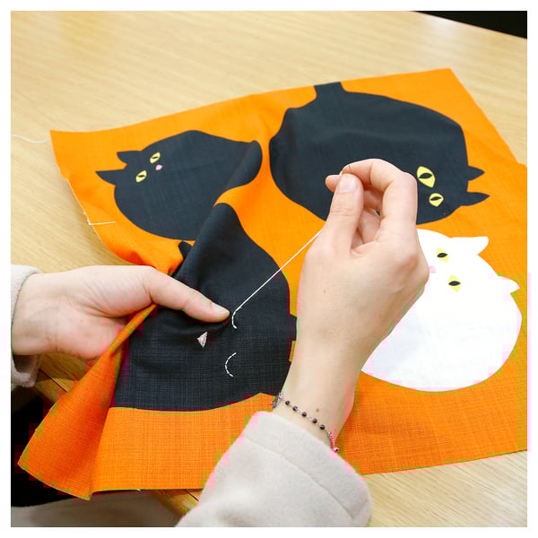 Hands sewing cat cushion, orange, black & white cats.
