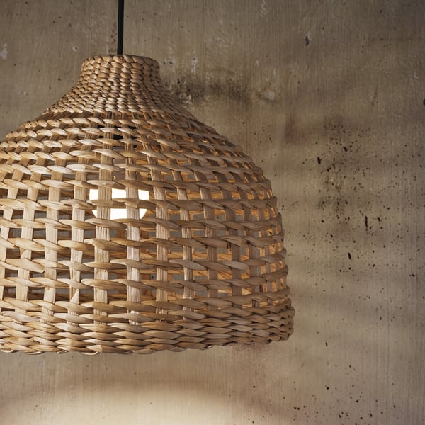 Rattan pendant light with intricate weave casts warm, soft glow, illuminating room; hangs from ceiling. Light visible through woven pattern.