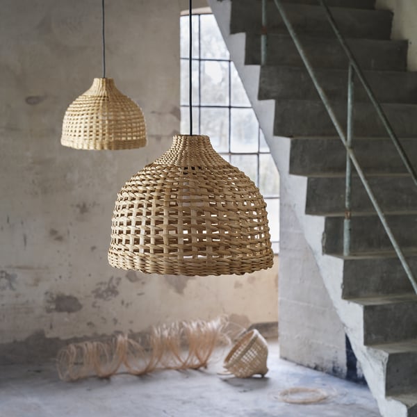 Two MÄVINN lamps hang near stairs, one large dome-shaped woven banana fibre lamp glows softly. Below, coiled material on wall emphasises its design.