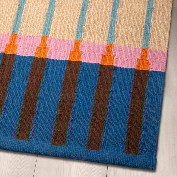 Brightly striped woven rug on wood floor. Blue, orange, pink, and beige stripes on jute base.