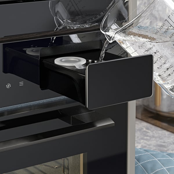 Modern oven with steam function, visible water dispenser pouring steam.