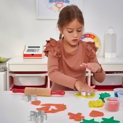 A young girl plays with MÅLA modelling dough, cutting shapes with included cutters, using a rolling pin.