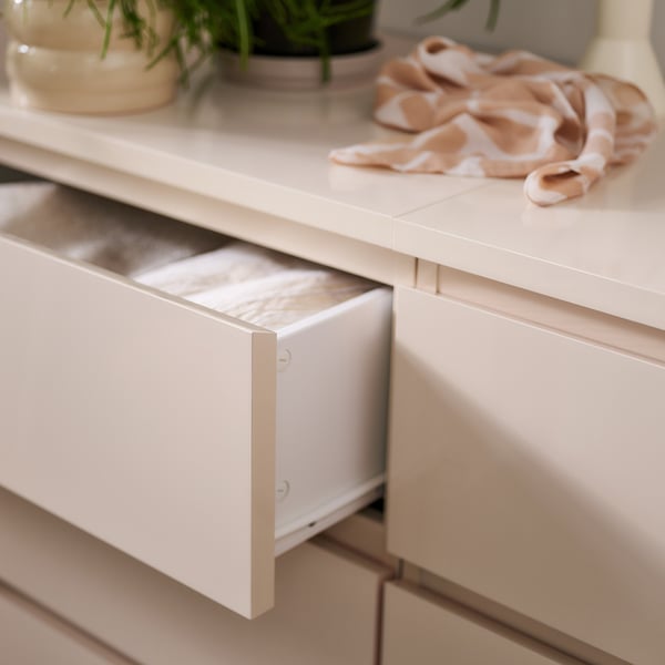 Modern light wooden drawer unit with open top drawer, decorated with plants and scarf.