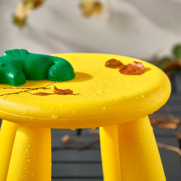 A yellow childrens stool with legs, wet from outdoors, holding leaf and toy shapes on top.