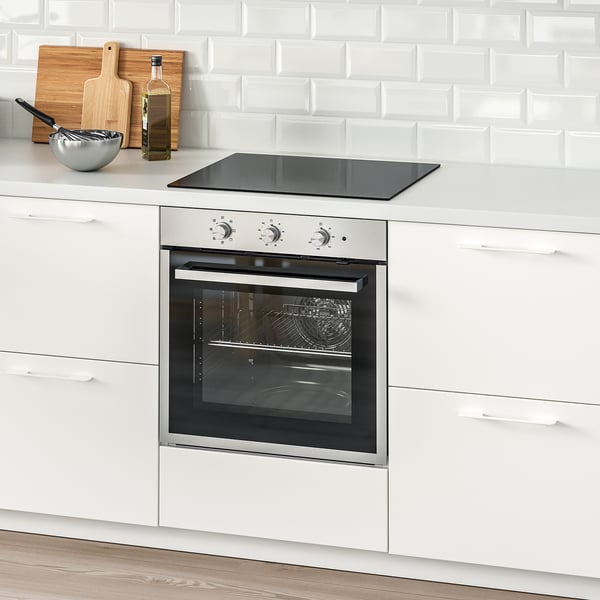 Modern kitchen: white, stainless steel oven, black cooktop, cutting boards, bottle.