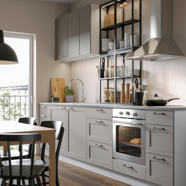 Modern kitchen with grey cabinets, stainless steel oven, and open shelves displaying dishes and utensils.