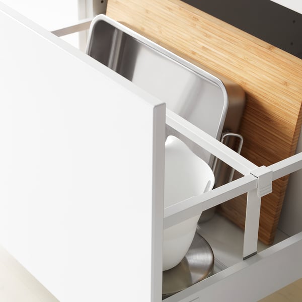 White kitchen drawer, fully extended, displaying aluminium trays and wooden cutting boards, highlighting organised storage.