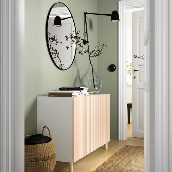 Modern living room with MEJARP sideboard, mirror, lamps, and basket of clothes against green wall.