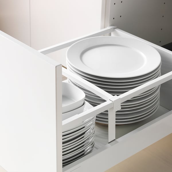 Open kitchen drawer revealing organised stacks of white plates and bowls, held by a metal divider for neat storage.