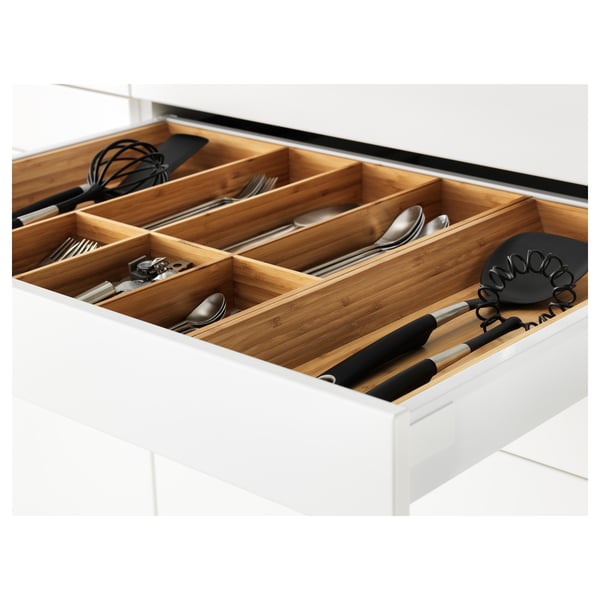A kitchen drawer with wooden organisers holding utensils and kitchen gadgets. It has a modern white finish, and the organisers are adjustable.