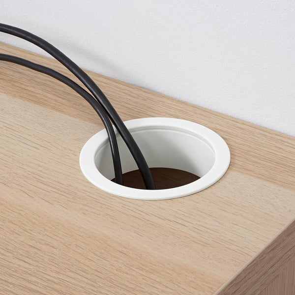 Wooden desk with a circular cable outlet, showing two black cables emerging from a white outlet, managing cable clutter.