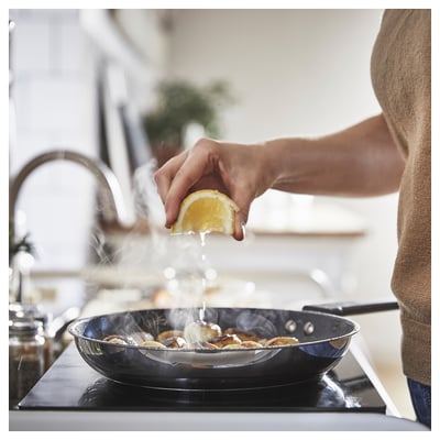 A chef squeezes lemon on a sizzling pan with food, steam rises.