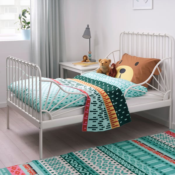 MINNEN metal bed with turquoise-green bedding and teddy bears. Nearby desk with lamp, colourful rug, light grey curtains.