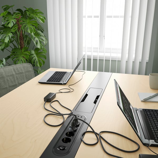 A modern conference table with built-in power sockets and cable management, ideal for business use, featuring four open laptops and a plant.