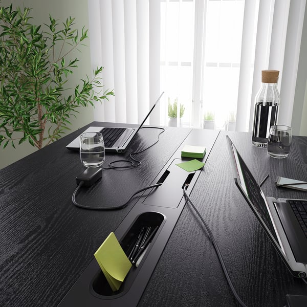 Modern high conference table with power outlets, cable management, and storage slots for pens and notes, suitable for sitting and standing.